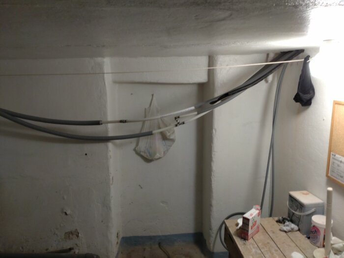 Oorganiserat utrymme med kablar, bord, mjölkkartong och hängande klädesplagg.