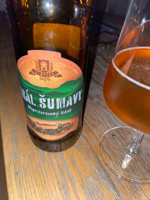 Ölflaska med etikett "IPA Sunava" och ölglas på träbord. Unpasteurized lager. Mysig stämning.