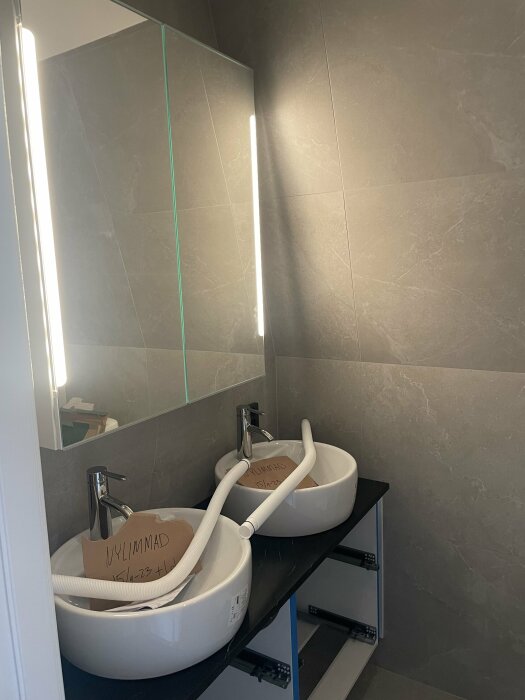 Modernt badrum med dubbla handfat, spegel och väggbelysning under installation eller reparation.