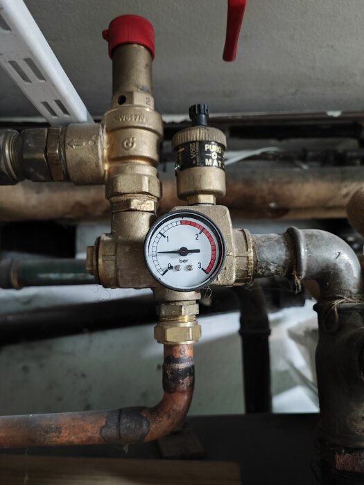 Tryckmätare på rörledning med ventiler och kopplingar, möjligen en del av VVS-installation eller uppvärmningssystem.