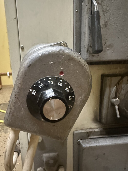 Äldre termometer på industriell utrustning, smuts, slitna detaljer, analog avläsning, temperatur mellan 60 och 70 grader.