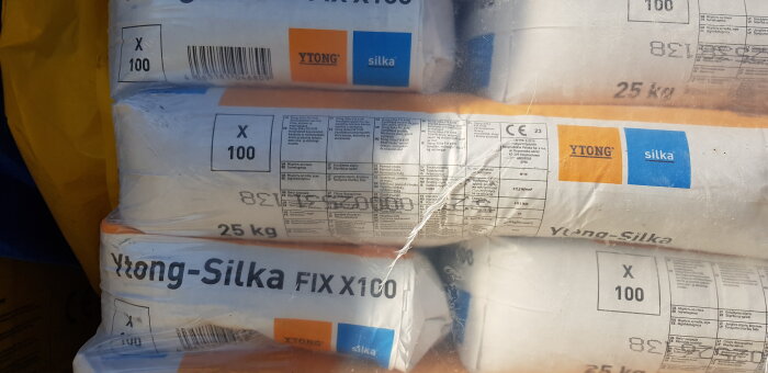 Staplar av förpackade Ytong-Silka Fix X100, byggmaterial, etiketter och specifikationer synliga, 25 kg varje.