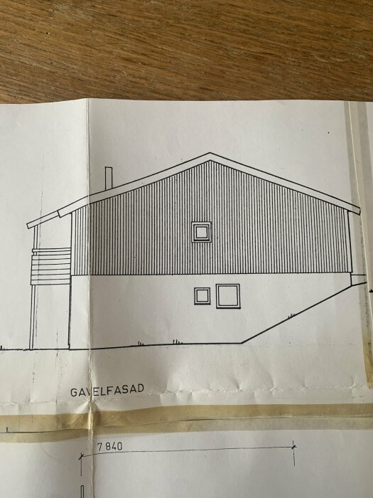 Arkitektritning av en husgavel med fönster, dörr och måttangivelser. Tecknat på papper, fotografi taget ovanifrån.