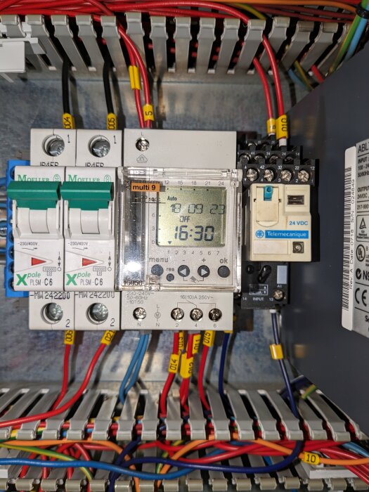 Elektriskt styrsystem med kabeldragningar, säkringar och en digital timer på en DIN-skena.