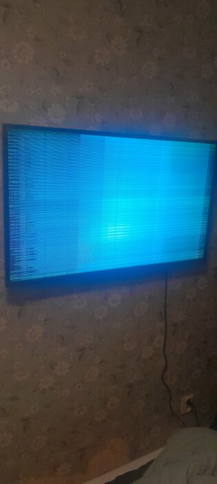 En TV visas med blå skärm och felmeddelande, hängd på tapetserad vägg.
