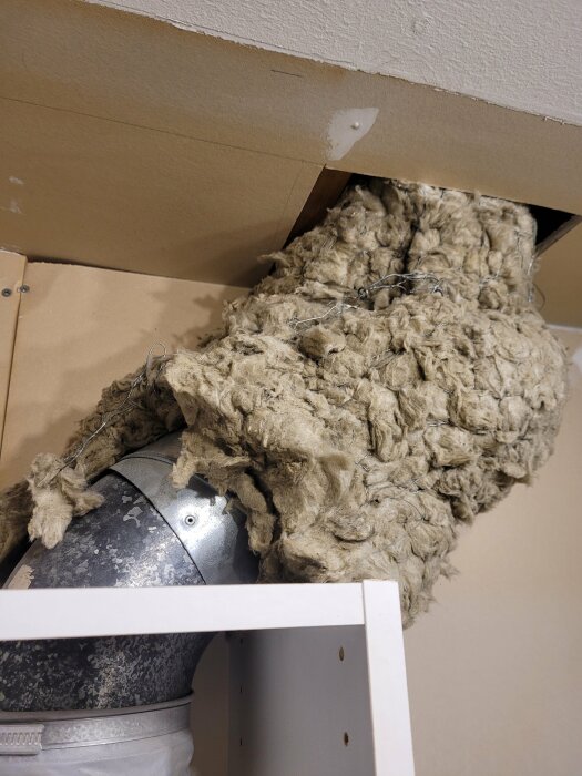 Isolering sticker ut från öppet utrymme i tak, nära luftkanal och träskelett, oordnat, renoveringsarbete.