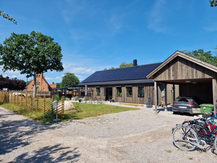 Lantlig scen med byggnader, solpaneler, kyrka i bakgrunden, cyklar, bil och blå himmel.