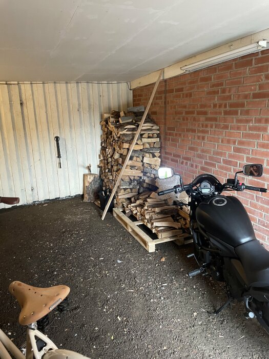 Träved staplad i garage, motorcykel, tegelvägg, träpanel, skottkärra, dämpad belysning, grusgolv, tak.