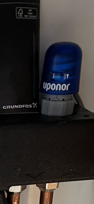 VVS-installation med Grundfos-enhet och blå Uponor-komponent monterade på en vägg ovanför kopparledningar.