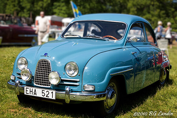 Blå klassisk bil på bilutställning under solig dag, människor i bakgrunden, svensk registreringsskylt.
