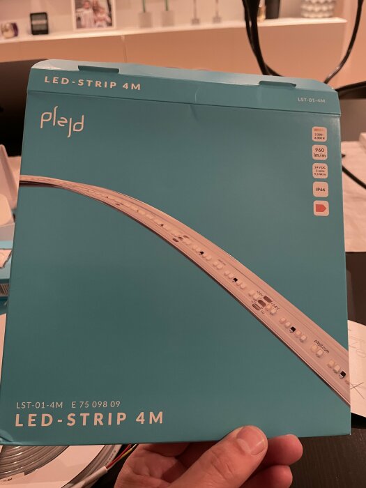 Förpackning för 4 meter LED-strip, teal färg, hålls i en hand, elektronikprodukt, IP66 märkt.