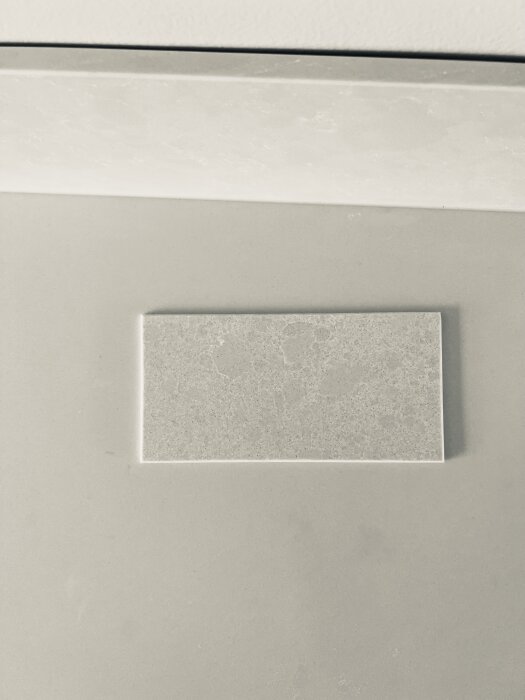 Svartvit bild på en rektangulär platta inramad i en vägg. Enkel, minimalistisk design.