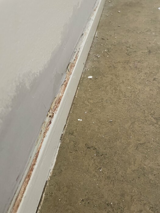 Vägg möter slitet golv; baseboard med fuktskador och mögel; renoveringsbehov.