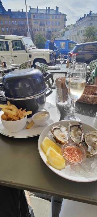 Musslor, pommes frites, sås och vin på utomhusservering i stadsmiljö, med gatuvy och fordon i bakgrunden.