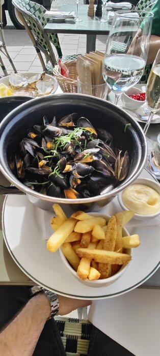 Moules-frites på restaurang: blåmusslor, pommes frites, majonnäs, vattenglas, utomhusmiljö, person med klocka.