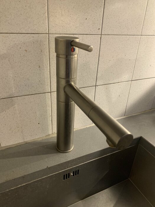 Rostfri vattenkran mot kakelvägg ovanför mörk handfat, modern design, inomhus, hygienutrustning.