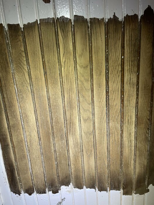 Slitet trä under flagnande vit färg på yta, troligen en vägg eller dörr. Nedslitet yttre, textur synlig.