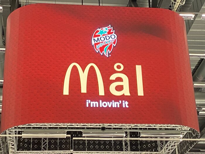 Stort rött skylt med bokstäverna "M" och "äl", slogan "I'm lovin' it", takkonstruktion i bakgrunden.