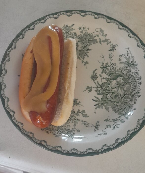 En hotdog med senap och ketchup på ett blommigt porslinstallrik.