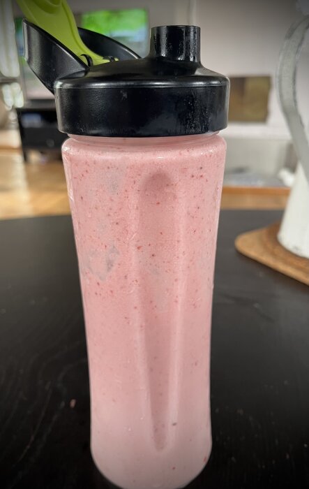 En shakerflaska fylld med rosa smoothie eller proteinshake på ett köksbord.