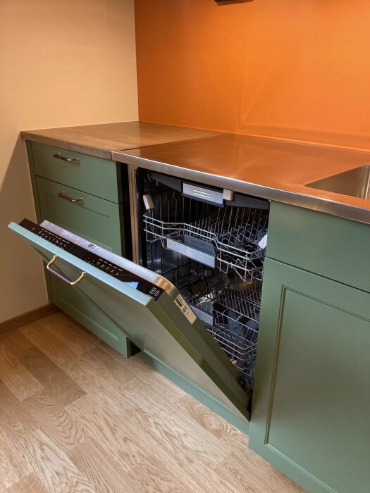 Integrerad diskmaskin halvöppen i ett modernt kök med trägolv och en orange vägg.