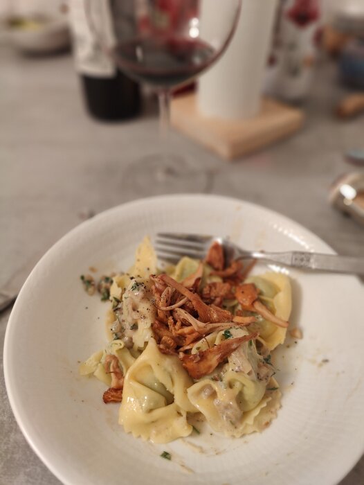 En tallrik med pasta och sås, toppad med örter och stekt svamp, vin i bakgrunden.