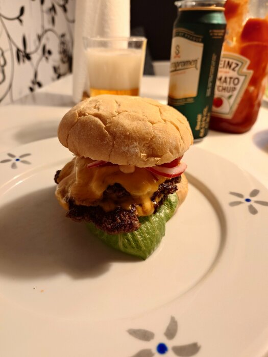 Hamburgare med bröd, ost, lök, salladsblad på tallrik; tomatketchup, ölburk och mjölkglas i bakgrunden.