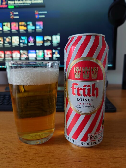 Ett glas öl bredvid en ölburk framför en datorskärm som visar musiktjänsten Spotify.