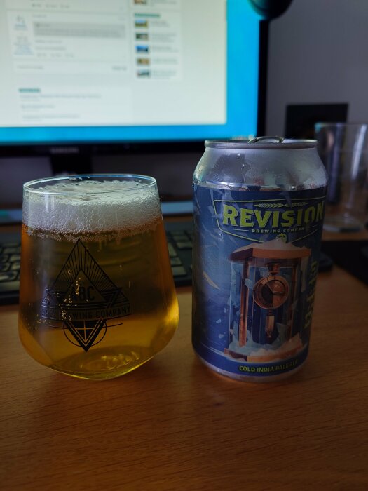 Öl i glas bredvid burk på skrivbord framför datorskärm. Bryggeri-logotyper synliga. Arbete och avkoppling teman.