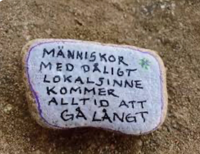 Sten målad med text: "Människor med dåligt lokalsinne kommer alltid att gå långt", sandig bakgrund.