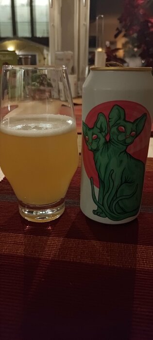 Glaset innehåller en grumlig vätska, troligen öl, bredvid en burk med konstnärlig design.