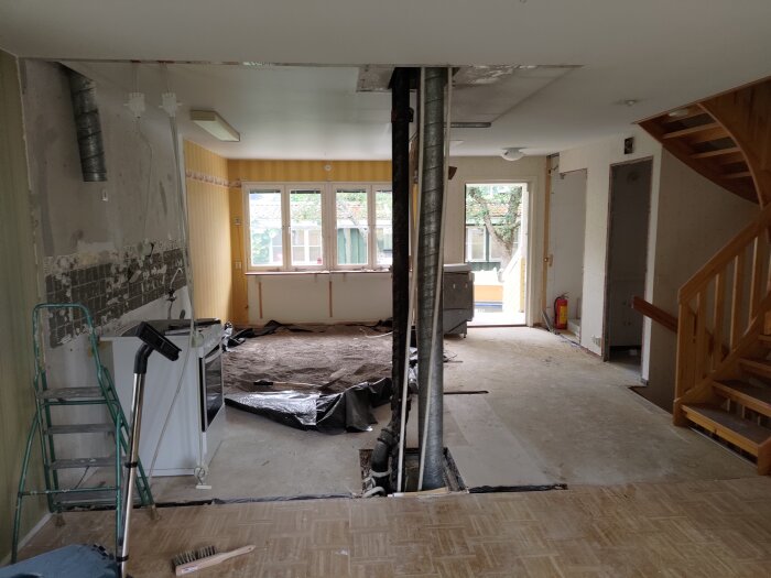 Renoveringsarbete pågår inne i tomt rum med synliga rör, tomma väggar och trapphus, oordning och byggmaterial synliga.