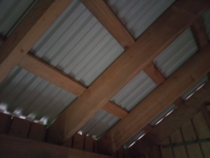 Takstruktur med träbjälkar och metallplåt, underifrånperspektiv, inomhus, suddig bild, svagt ljusinsläpp.