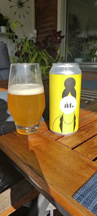 Ett glas med ljus öl och en burk på ett träbord utomhus. Sunny day.