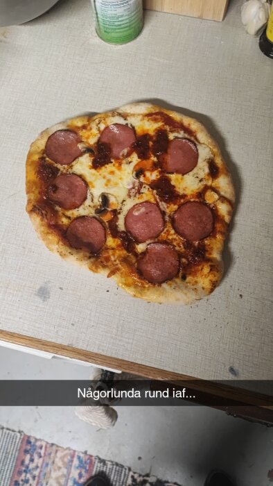 Hemgjord pizza med salami ovanpå, oregelbunden form, texten säger "Någorlunda rund iaf...".