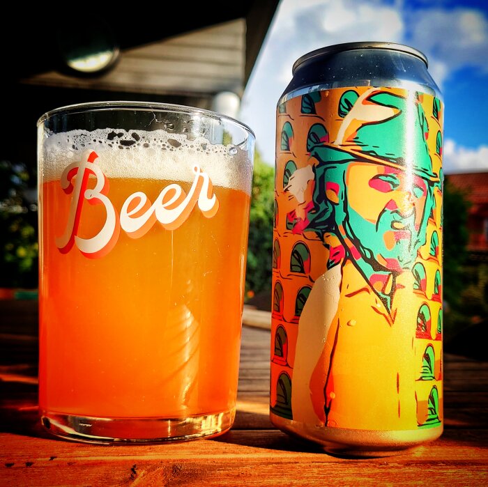 Ett glas öl bredvid en färgglad ölburk utomhus i solnedgångens ljus.