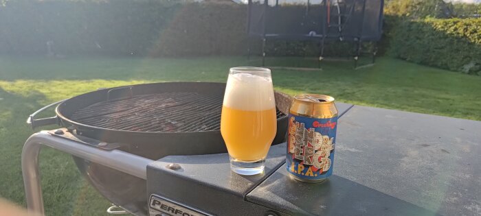 Grill i trädgård, ölglas och burk, soligt, avkopplande sommarkväll.