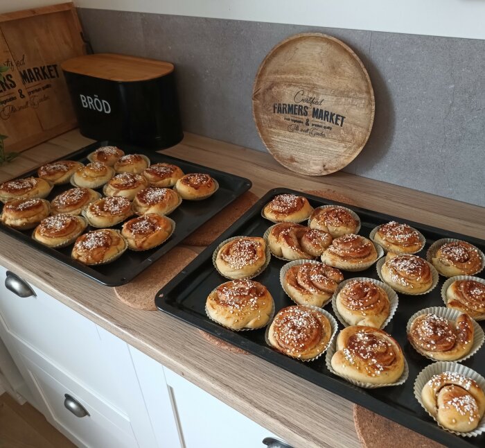 Nybakade bullar på köksbänk, strösocker ovanpå, kakformar, träskylt i bakgrunden, mysigt hemkök.