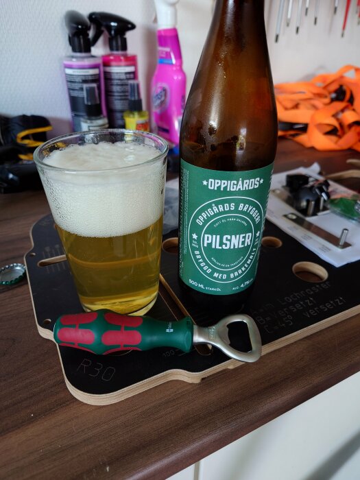 Ölglas på bord, Oppigårds bryggeriflaska, skruvmejsel, verktygstavla, måttsats, sprayflaskor i bakgrunden.