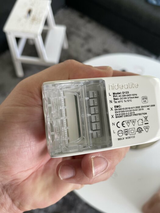 Hand håller en elektrisk komponent, genomskinlig kapsling, modellinformation, inomhusmiljö.