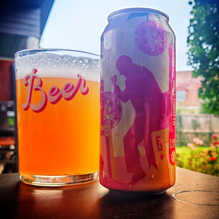 Ett glas öl och en konstnärligt designad burk utomhus på en bordsskiva.