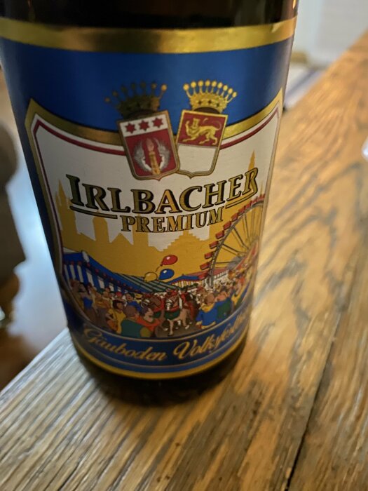 Ölflaska med etikett "Irlbacher Premium", vapensköldar, folk på karusell, text "Bayerische Festtradition".