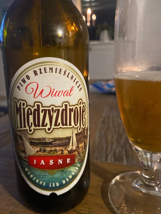 Ölflaska och glas på ett bord, troligtvis artisant öl, polsk text, mysig atmosfär.