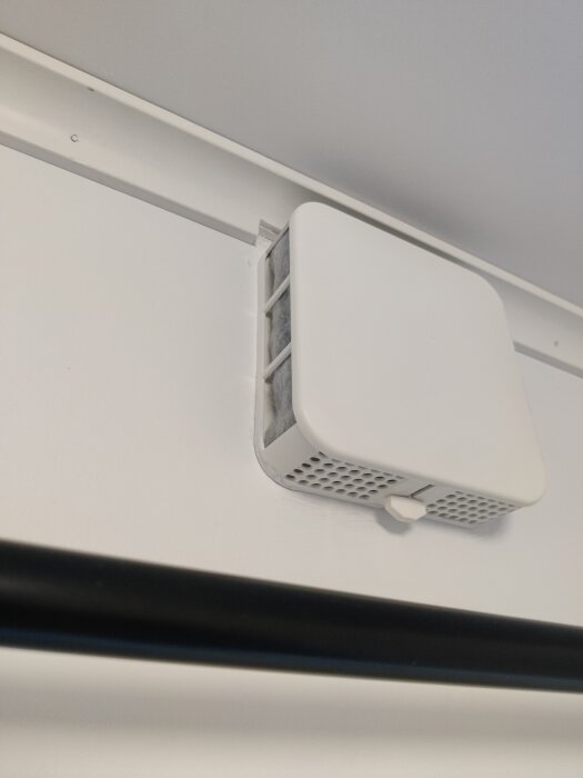 Vit Wi-Fi-router monterad på vägg, delvis ovanför taklist med synlig antenn och kablar.