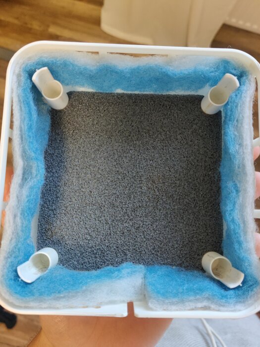 En uppochnedvänd tom bläckpatronsförpackning med blått kvarstående bläck och fyra plastfästen.