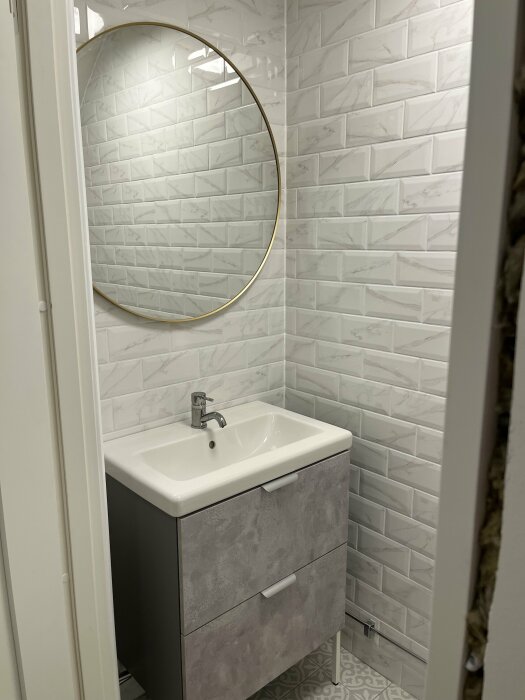 Modernt badrum med handfat, spegel, kakelväggar och mönstrat golv.