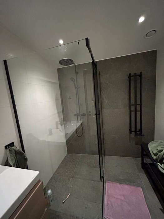 Modernt badrum, duschutrymme med glasväggar, handduksvärmare och grått golv.