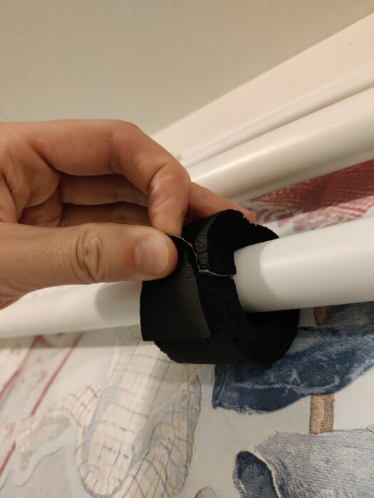 Hand monterar svart fäste på vit rörstruktur, textil bakgrund.
