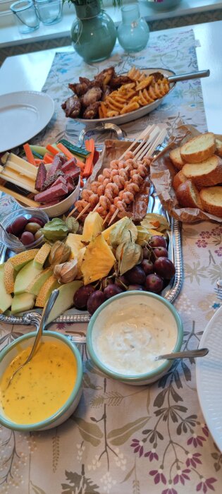 Ett dukat bord med blandade förrätter: charkuterier, räkor, bröd, ost, dipsåser och färsk frukt.