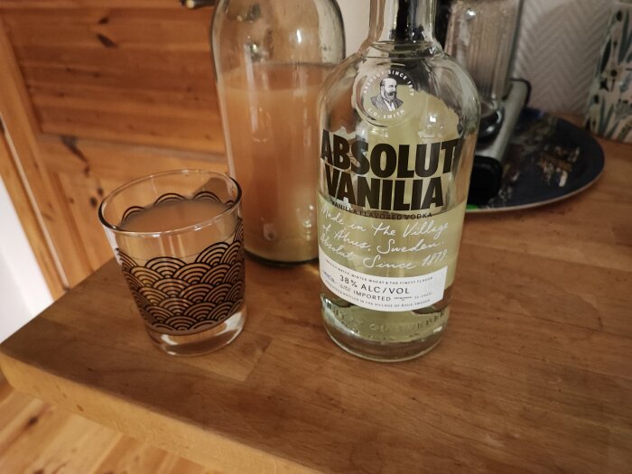 Absolut Vanilia vodkaflaska, mönstrat glas, köksinredning, trämöbler, inomhusmiljö.